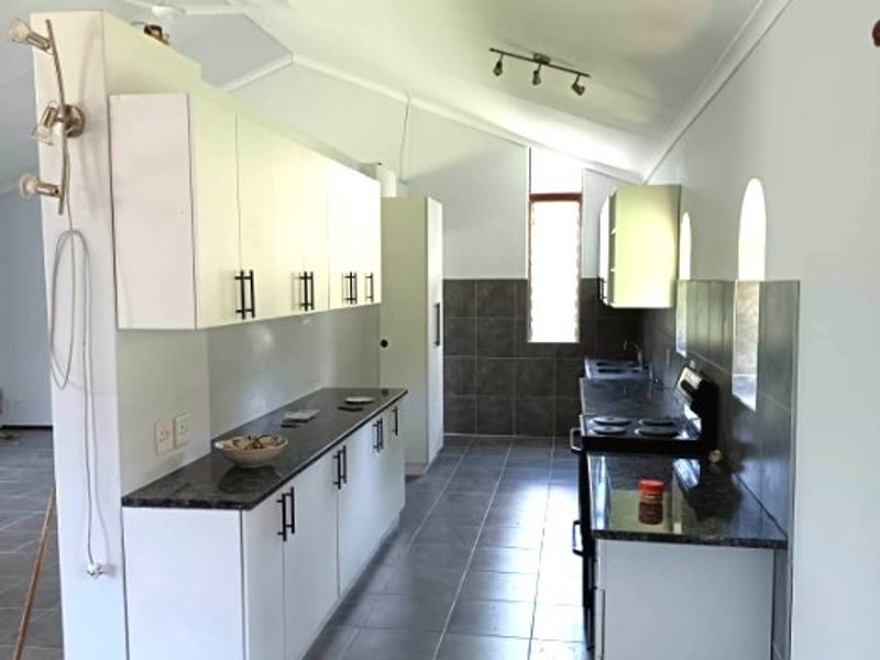 A clean, functional kitchen featuring white cabinetry, dark granite countertops, tiled flooring, and a vaulted ceiling with track lighting.