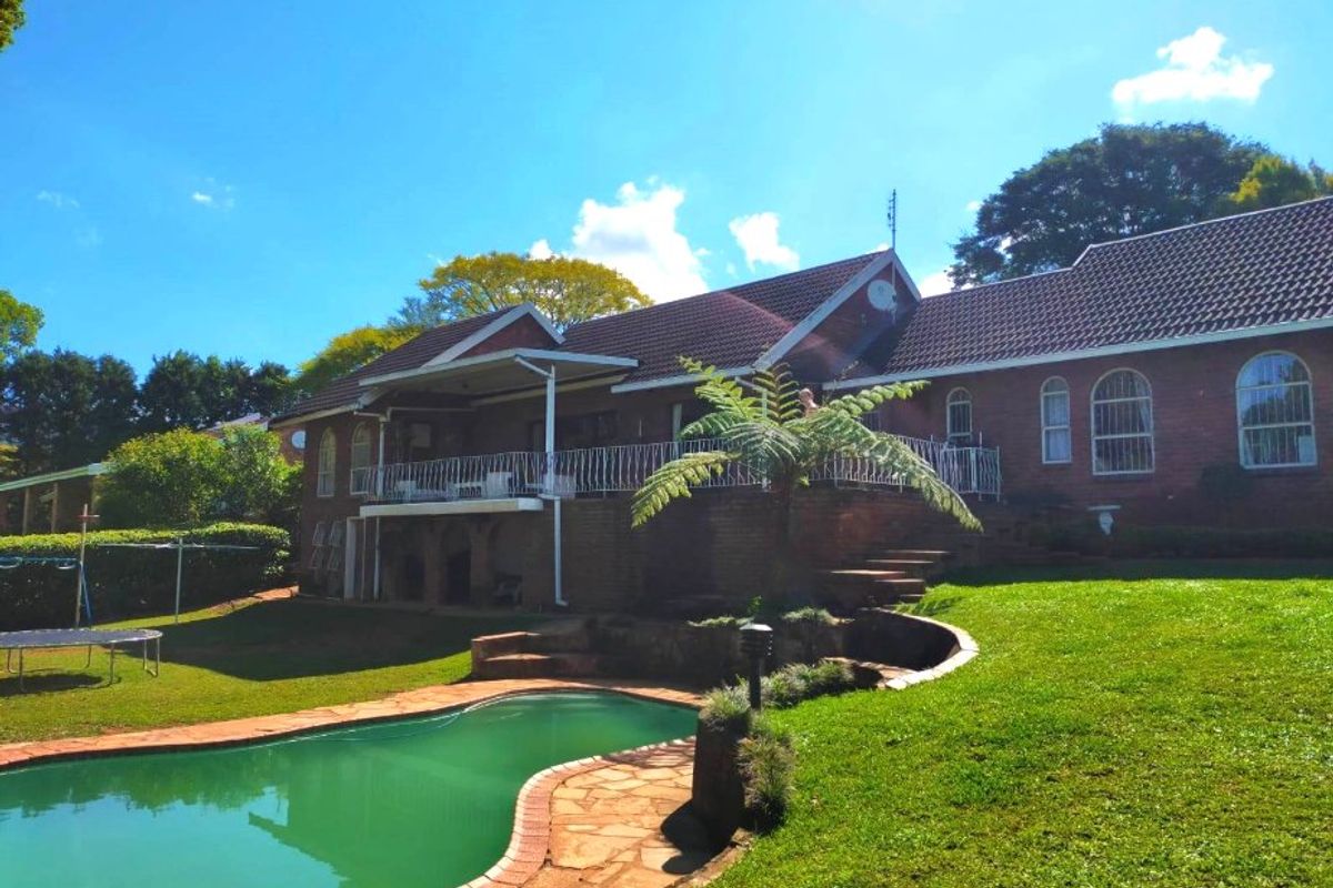 Rear view of a brick house featuring a swimming pool, raised patio with wrought iron balustrade, and a well-maintained garden.