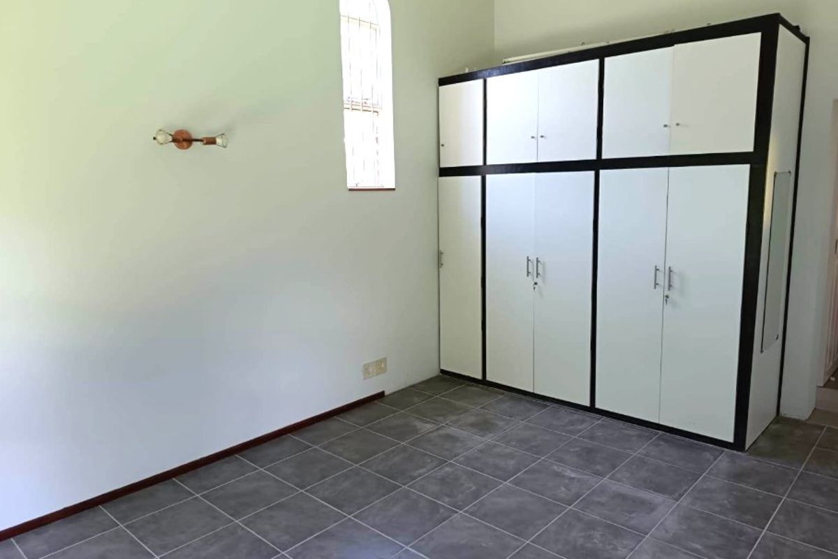 A clean, empty bedroom featuring tiled flooring, a distinctive arched window, and ample built-in cupboard storage space.