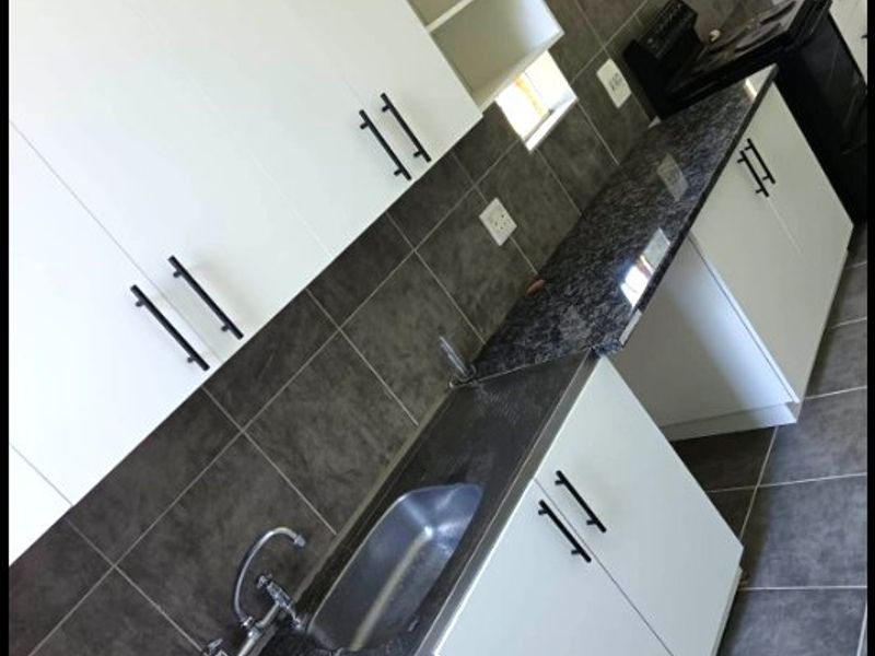 A modern kitchen featuring white cabinetry, dark granite countertops, a stainless steel double sink, and tiled backsplash and flooring.