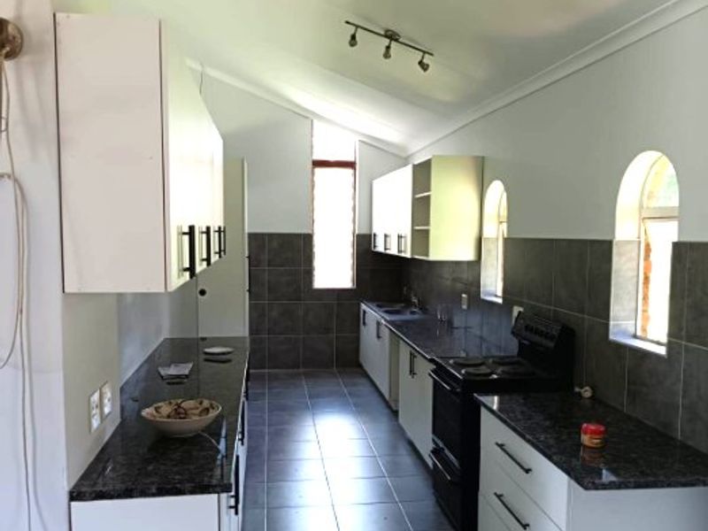 A galley-style kitchen featuring granite countertops, tiled backsplash, ample cabinetry, and a freestanding stove, illuminated by track lighting and natural light from arched windows.