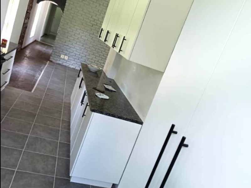 Modern kitchen featuring white cabinetry, dark stone countertops, and grey tiled flooring, complemented by an exposed brick feature wall.