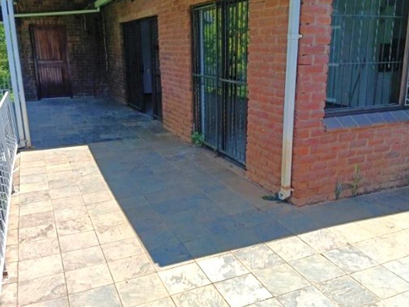 A paved outdoor patio area featuring brick exterior walls, security gates, and a covered section, offering a functional space for outdoor living.