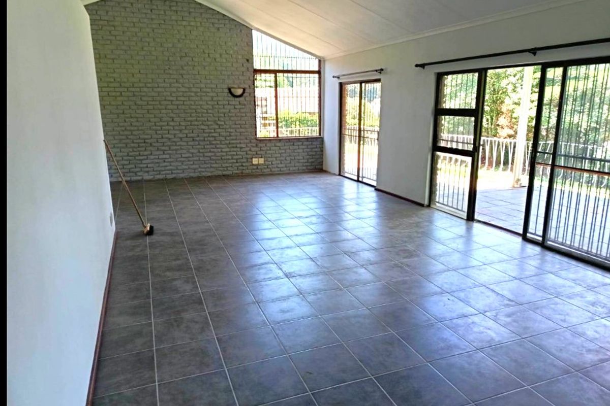 Spacious living area featuring tiled floors, a vaulted ceiling, an exposed brick feature wall, and large sliding glass doors leading to an outdoor space.