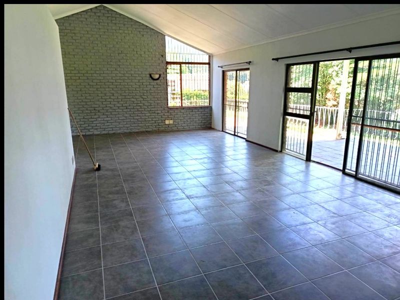 Spacious living area featuring tiled floors, a vaulted ceiling, an exposed brick feature wall, and large sliding glass doors leading to an outdoor space.