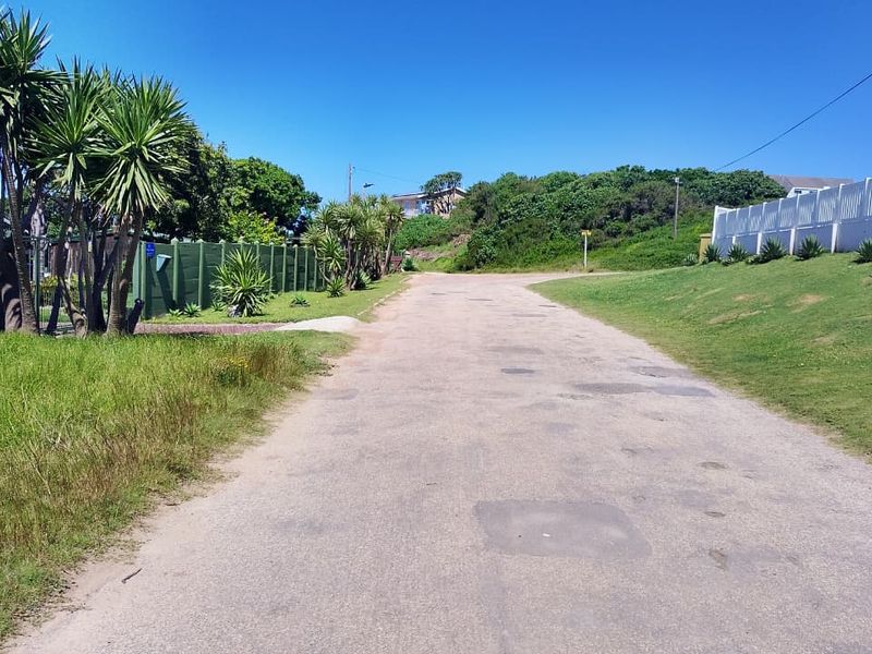 A view of the residential street access featuring an asphalt road, boundary fencing, and established landscaping along the verge.