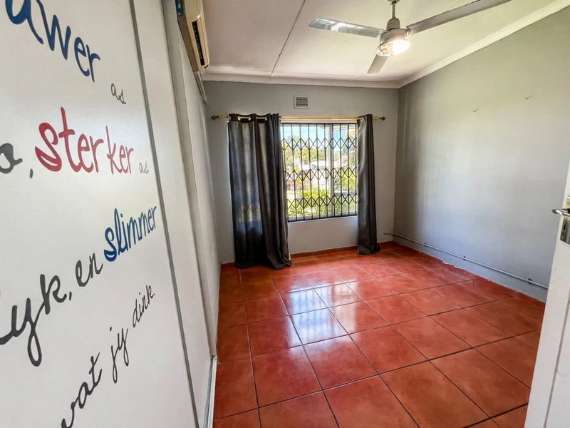 A vacant bedroom featuring tiled flooring, a ceiling fan, an air conditioning unit, and a security gate on the window.