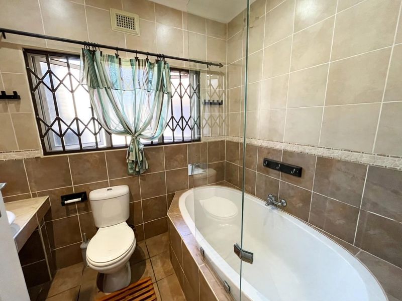 A functional bathroom featuring a built-in bathtub with a glass screen, tiled walls, and a toilet, finished with neutral ceramic tiling.