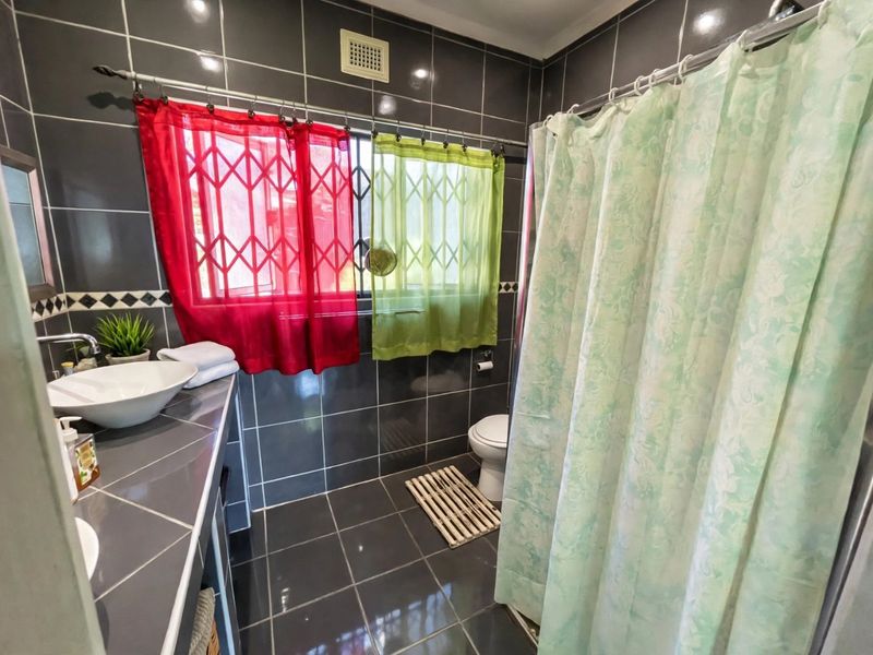 A functional bathroom featuring dark tiled walls and flooring, a vessel sink on a tiled vanity, and a shower area with a curtain.