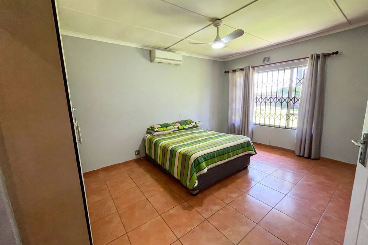 A functional bedroom featuring tiled flooring, a ceiling fan, a wall-mounted air conditioning unit, and a security gate over the window.