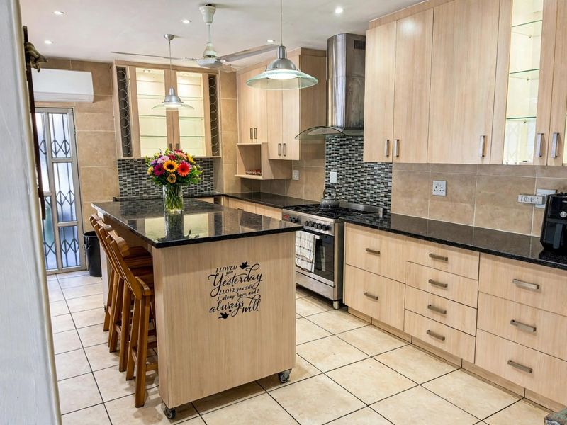 Modern kitchen featuring light wood cabinetry, granite countertops, stainless steel appliances, tiled backsplash, and a functional island with breakfast seating.