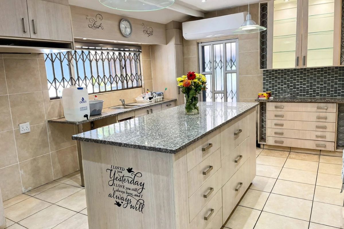 A spacious kitchen featuring a central island with granite countertops, extensive built-in cabinetry, glass display units, and tiled flooring throughout.