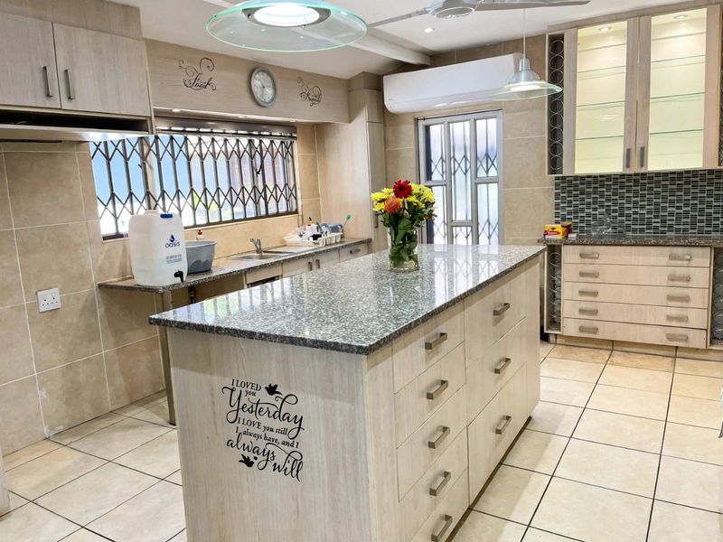 A spacious kitchen featuring a central island with granite countertops, extensive built-in cabinetry, glass display units, and tiled flooring throughout.