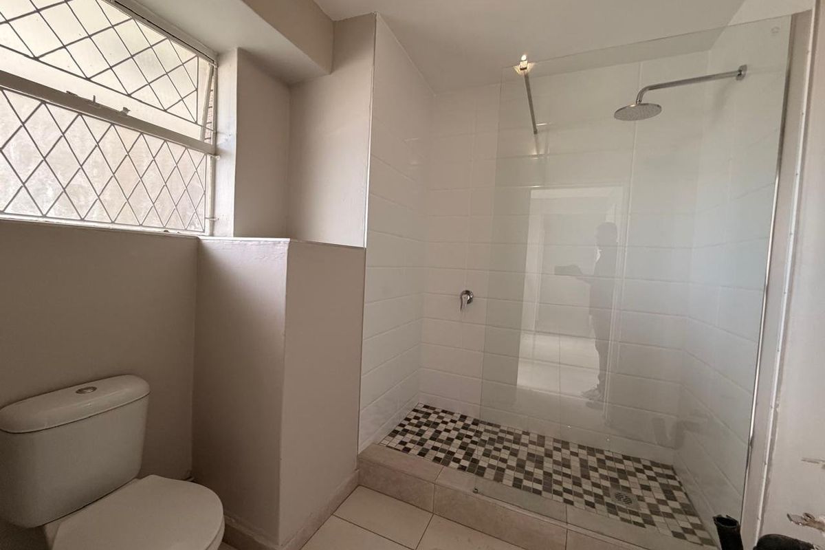 A functional bathroom featuring a walk-in shower with a glass screen, tiled finishes, and a standard toilet.