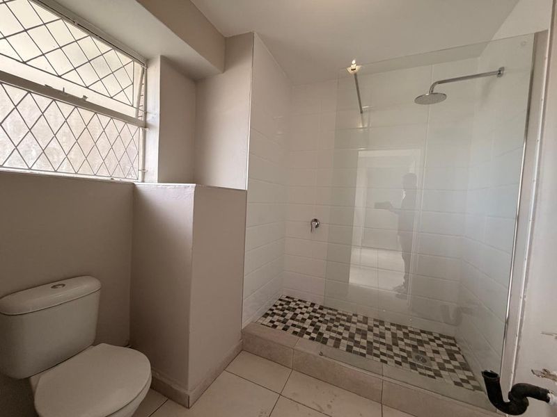 A functional bathroom featuring a walk-in shower with a glass screen, tiled finishes, and a standard toilet.