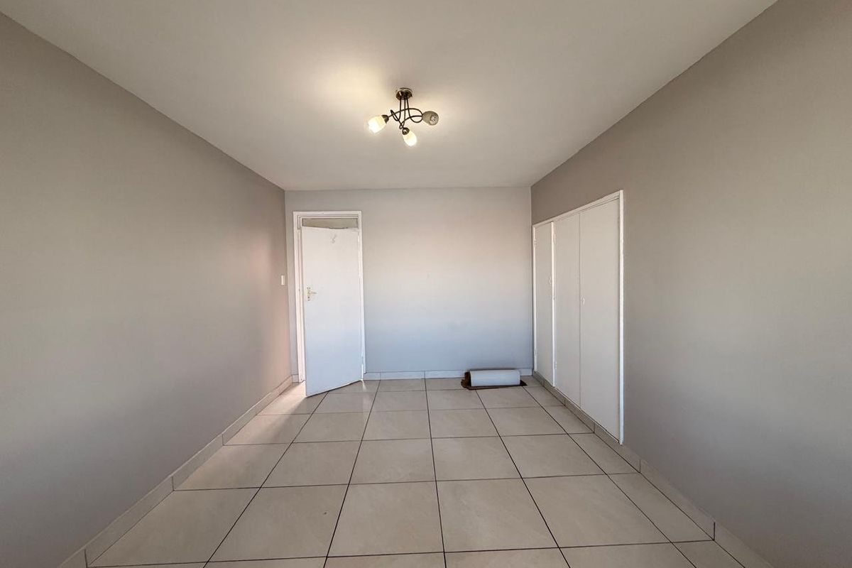An empty bedroom featuring neutral wall paint, tiled flooring, and built-in storage cupboards.