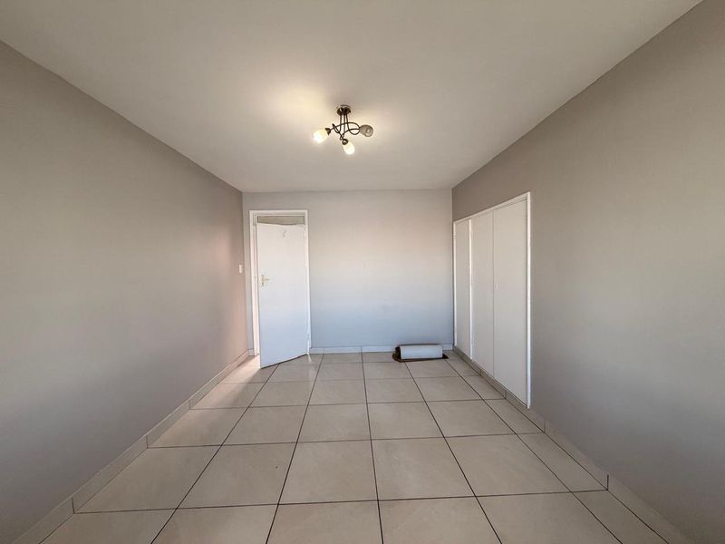 An empty bedroom featuring neutral wall paint, tiled flooring, and built-in storage cupboards.