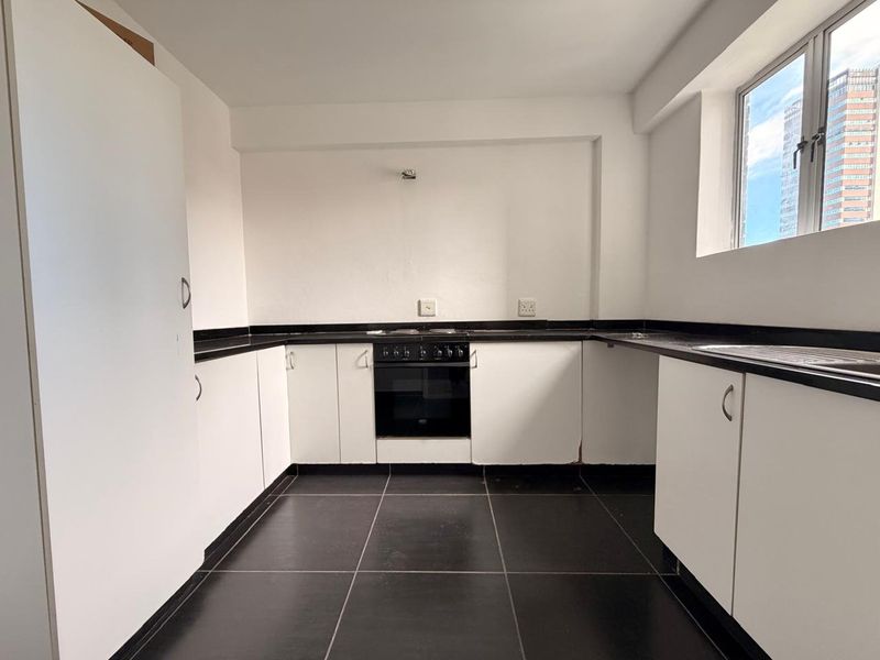A functional kitchen featuring white cabinetry, black granite countertops, tiled flooring, and a built-in oven with hob.