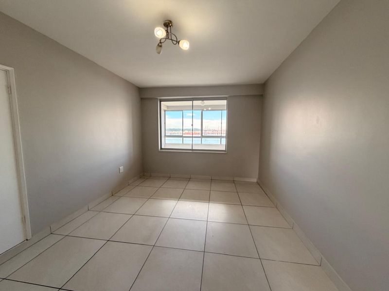 An empty bedroom featuring neutral tiled flooring, a sliding window with a view, and a central ceiling light fixture.