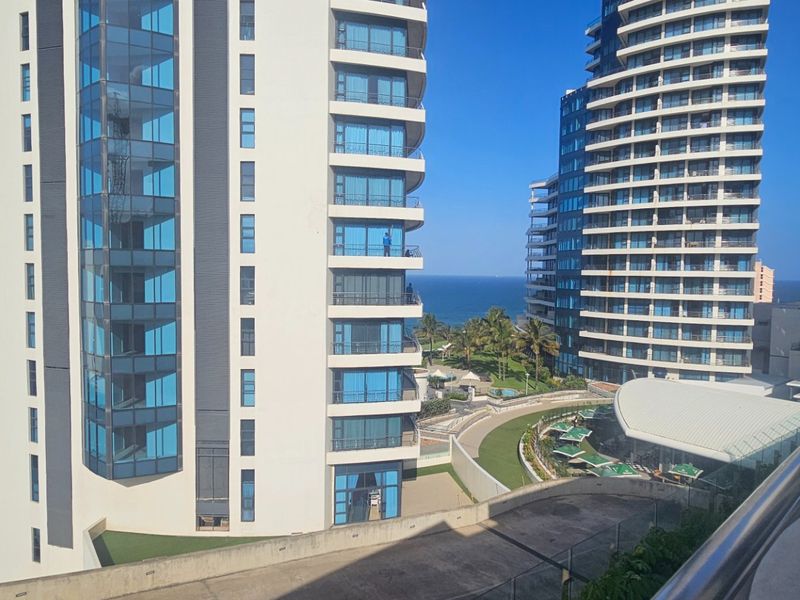 Elevated view overlooking modern apartment towers, landscaped grounds, and the ocean horizon from a balcony.