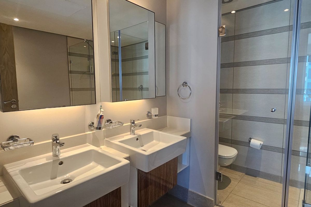 Modern bathroom featuring a double vanity with under-mount sinks, wall-mounted mirrors, and a spacious glass-enclosed shower with contemporary tiled finishes.