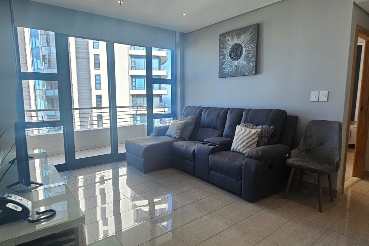 A modern living room featuring polished tiled flooring, recessed lighting, and large sliding glass doors providing access to a balcony with urban views.