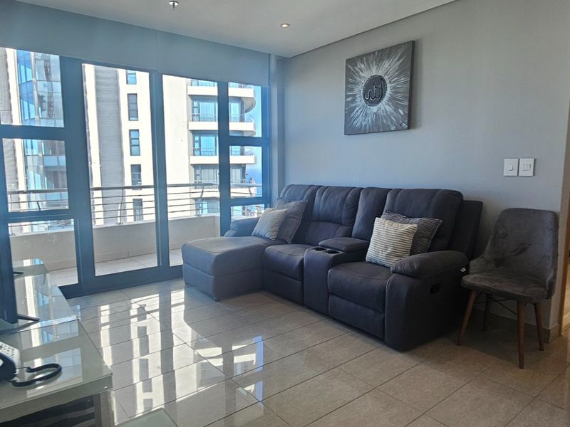A modern living room featuring polished tiled flooring, recessed lighting, and large sliding glass doors providing access to a balcony with urban views.