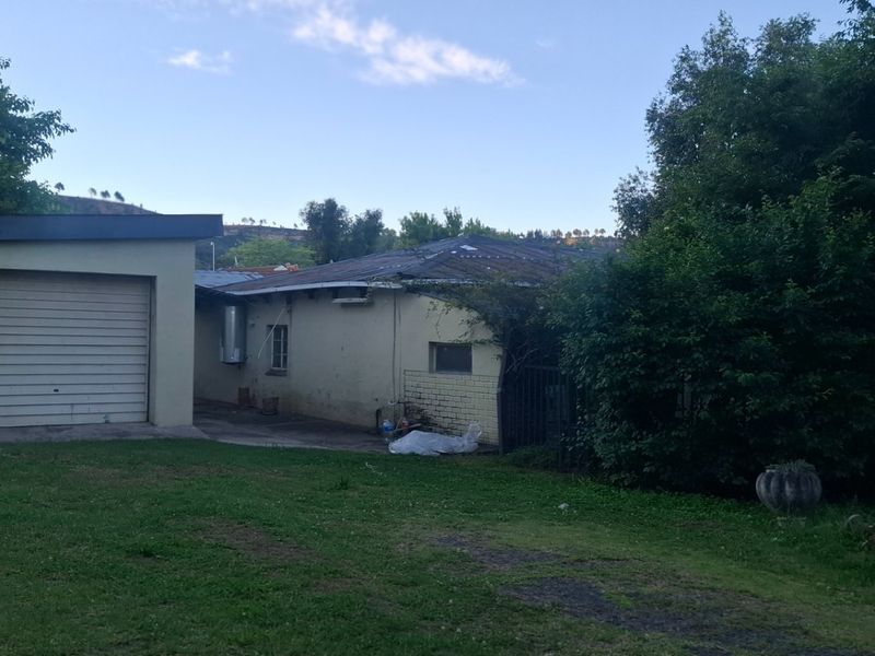 Rear view of the property showing a detached garage, brick exterior walls, and a large garden area requiring maintenance.