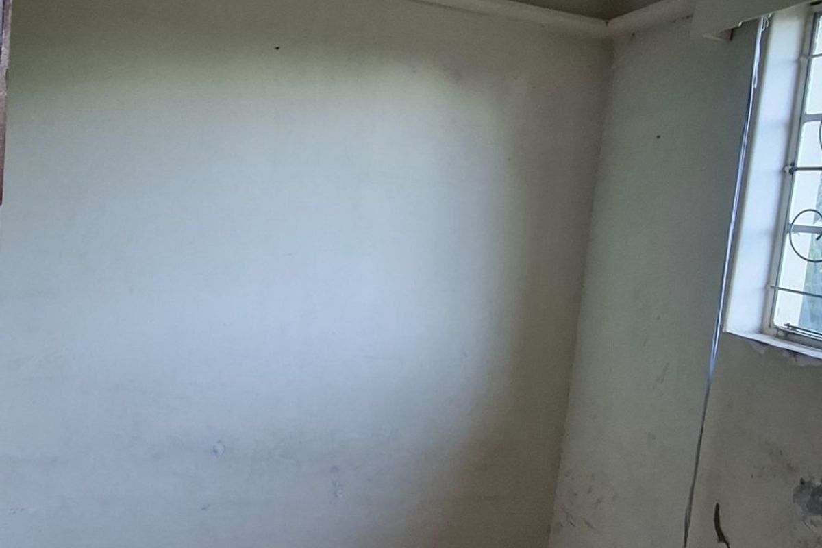 An empty bedroom featuring tiled flooring and security bars on the window, requiring cosmetic updates to the walls and ceiling.