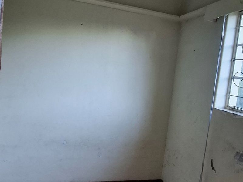 An empty bedroom featuring tiled flooring and security bars on the window, requiring cosmetic updates to the walls and ceiling.
