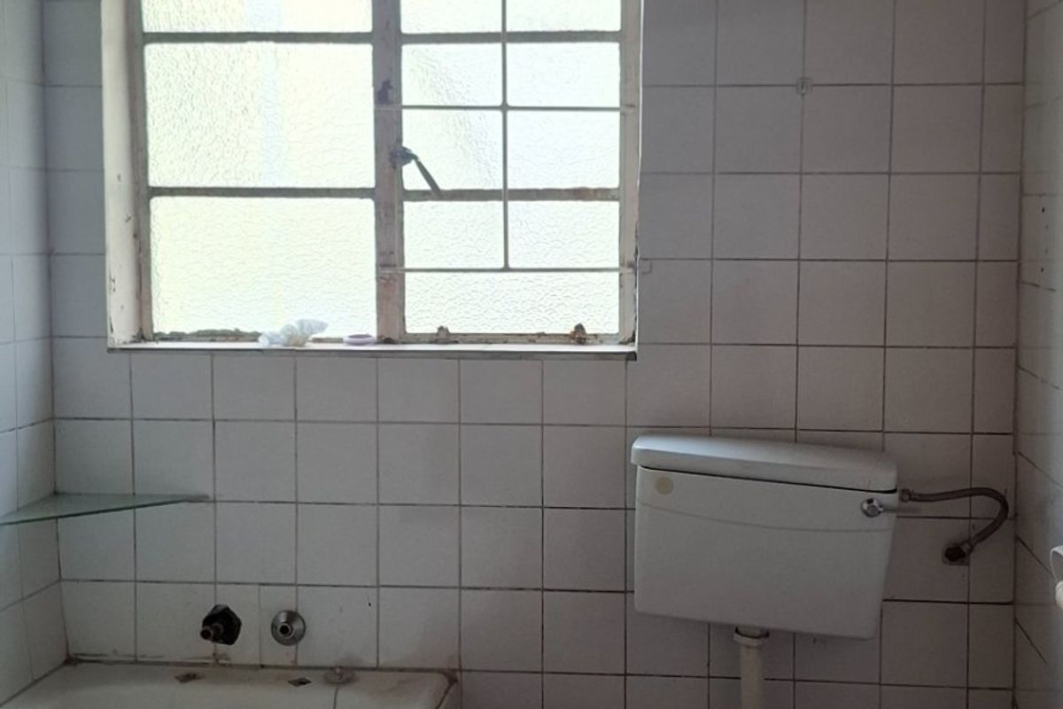 A dated bathroom featuring a standard bathtub, toilet, and tiled finishes, requiring modernization and refurbishment of fixtures and surfaces.