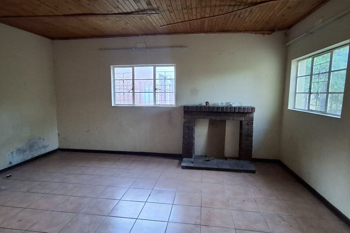 An empty living room featuring a brick fireplace, tiled flooring, and a timber ceiling, requiring cosmetic updates and wall repairs.
