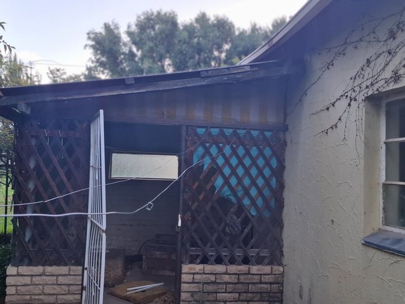 Rear exterior view showing a covered patio area with lattice screening, brick base, and security features on the main building structure.