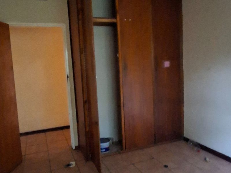 An empty bedroom featuring tiled flooring and built-in wooden cupboards, requiring cosmetic updates and repairs to the ceiling and lighting.