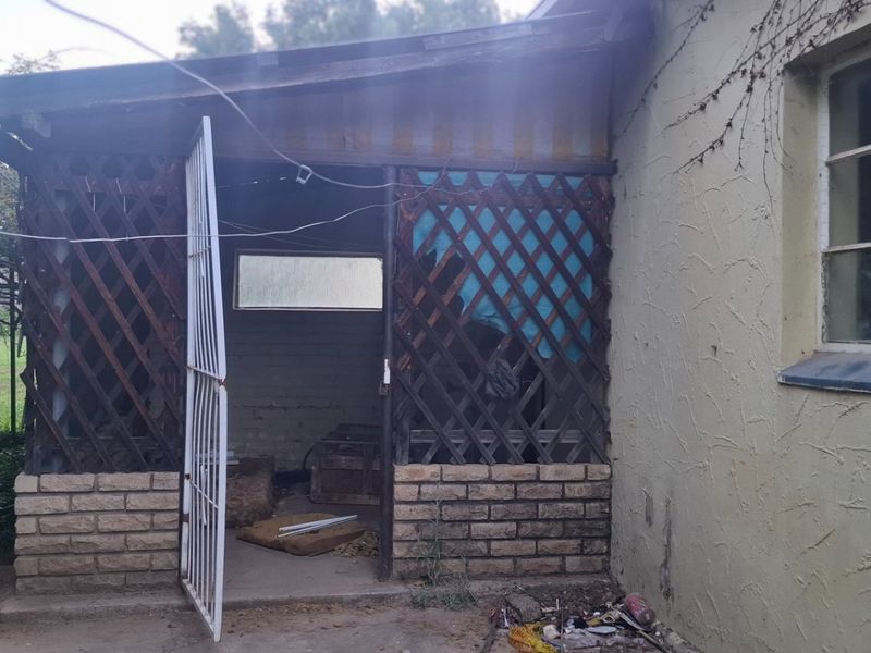Rear exterior view showing a weathered patio area with lattice screening, brick base, and a metal security gate requiring maintenance.