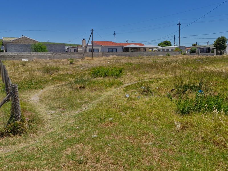 A vacant residential plot featuring a level grass surface, boundary fencing, and surrounding neighborhood views, ideal for new construction.