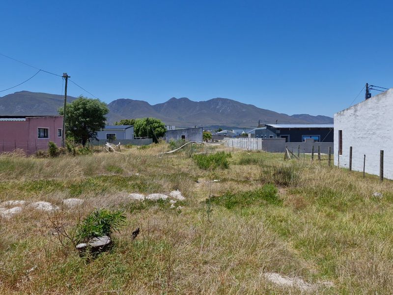 Vacant residential land with surrounding fencing and utility infrastructure, featuring mountain views in the background.