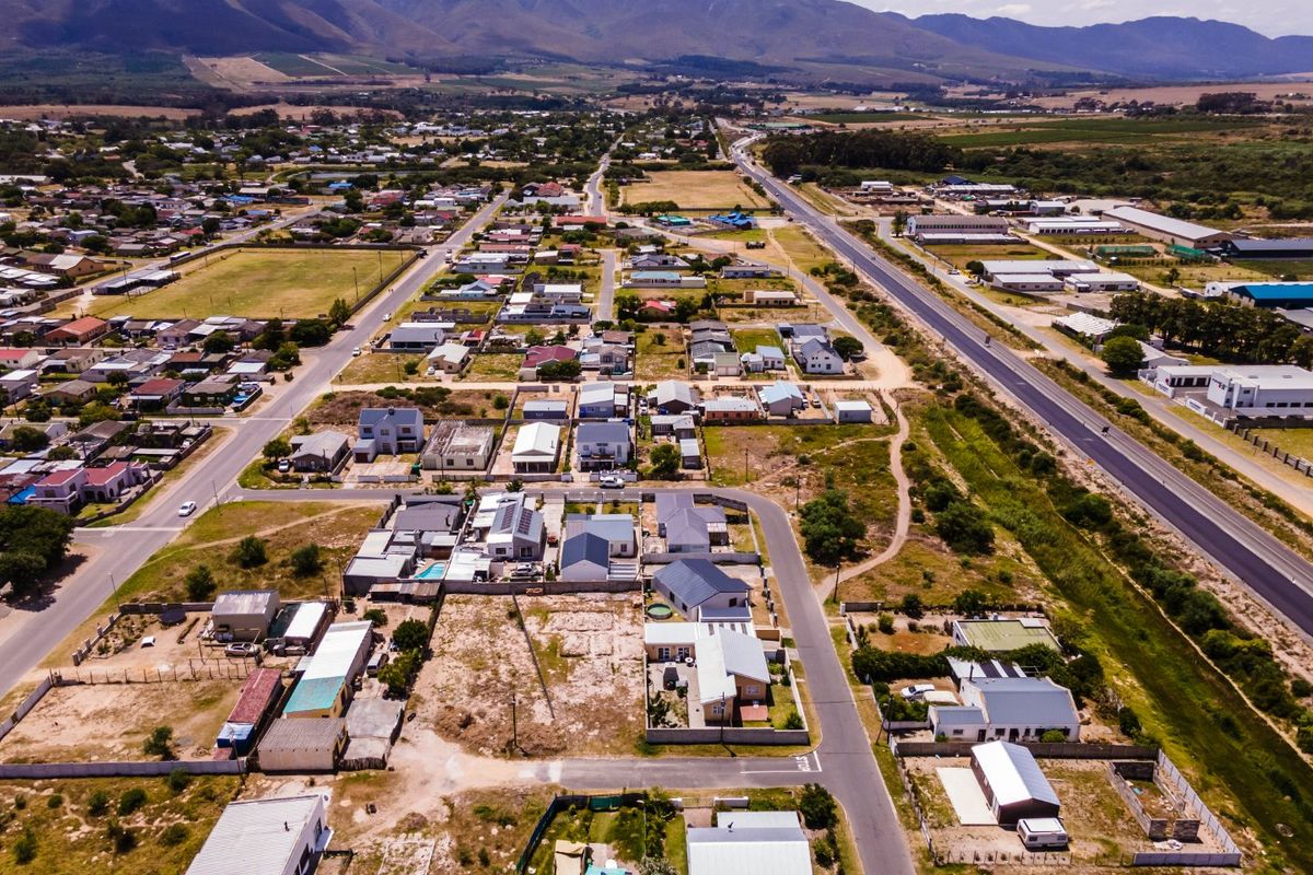 An aerial view of a residential neighborhood featuring vacant land plots, established housing, and scenic mountain views in the background.