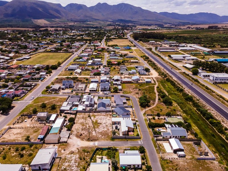 An aerial view of a residential neighborhood featuring vacant land plots, established housing, and scenic mountain views in the background.