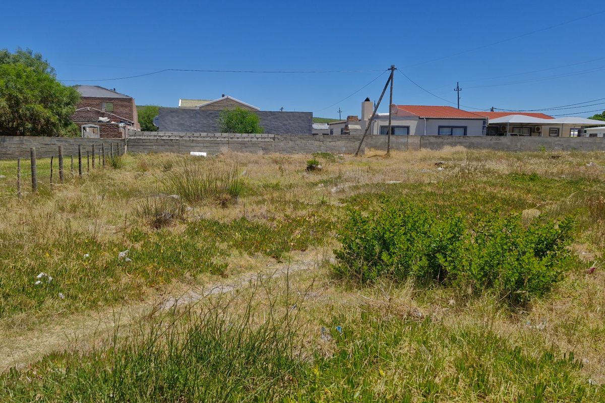 A vacant residential plot featuring a boundary wall, wire fencing, and natural vegetation, situated in an established neighborhood.