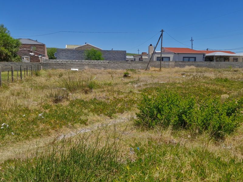 A vacant residential plot featuring a boundary wall, wire fencing, and natural vegetation, situated in an established neighborhood.