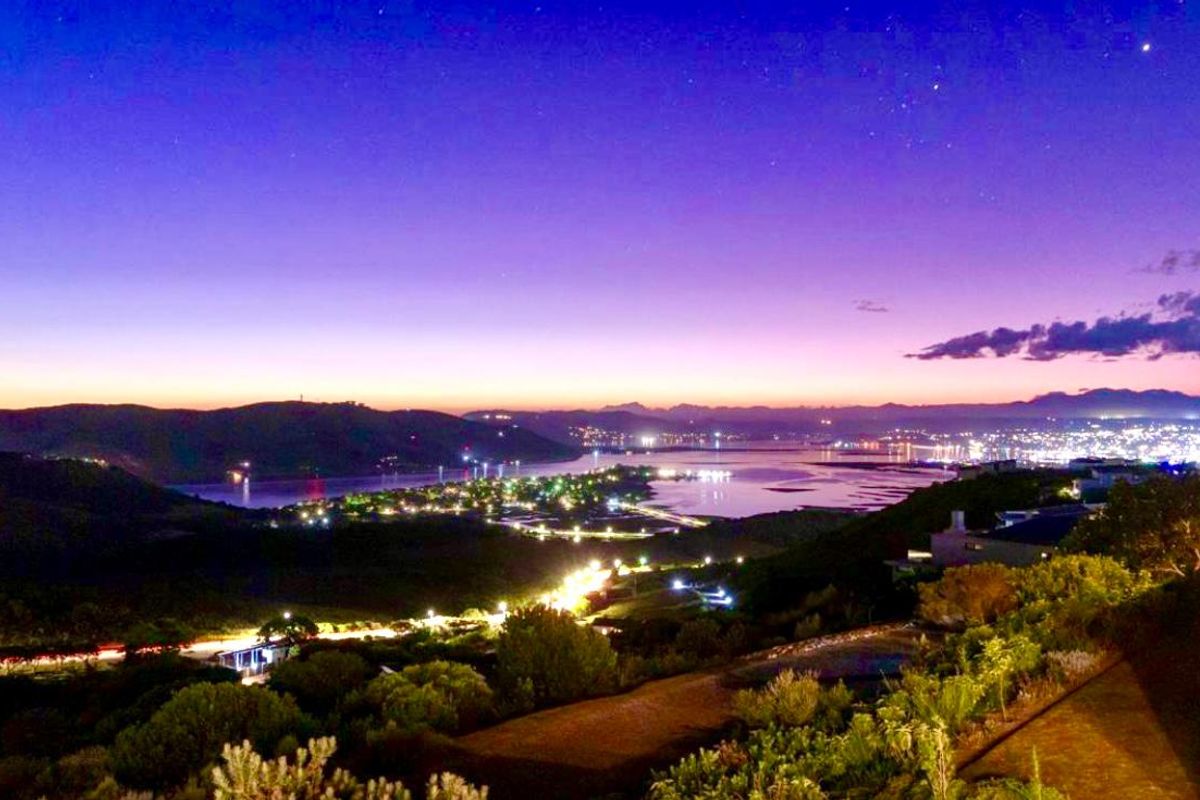 A stunning elevated night view overlooking the coastal landscape, lagoon, and illuminated town lights at dusk.