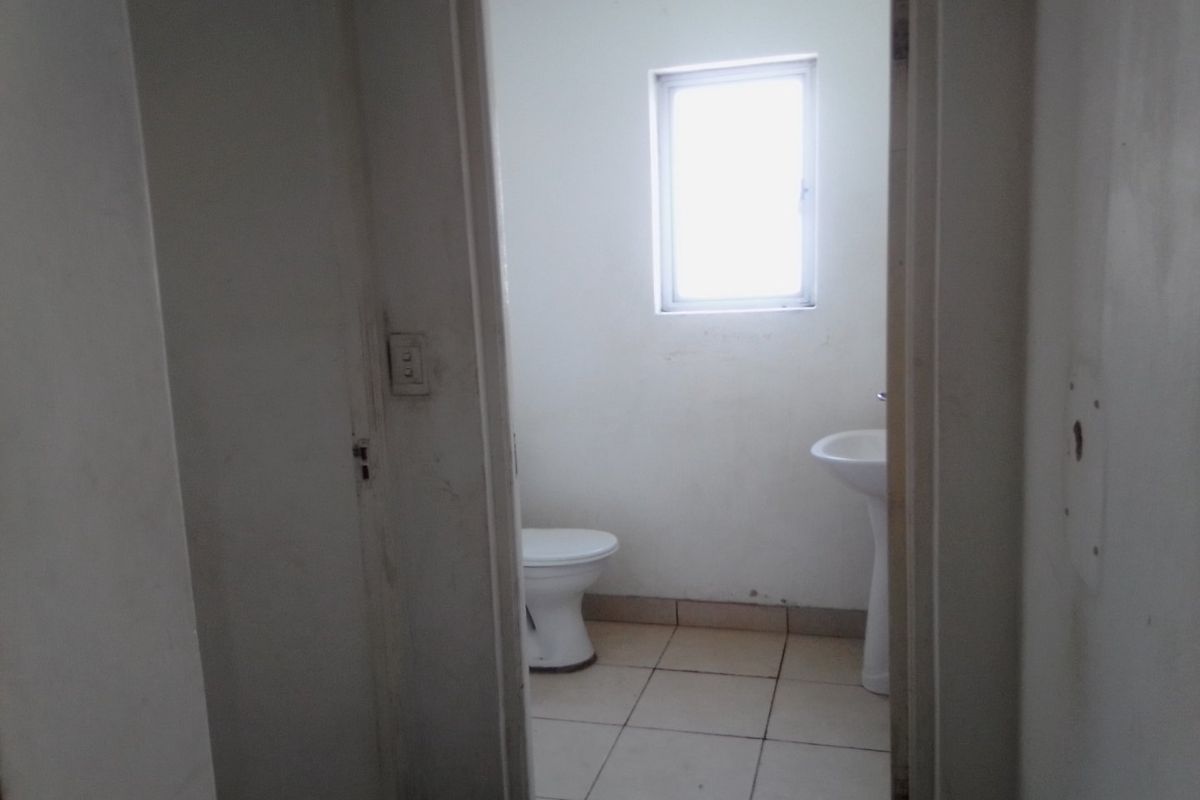 A small, functional bathroom featuring a pedestal basin, toilet, and tiled flooring, requiring cosmetic updates to improve its overall condition.
