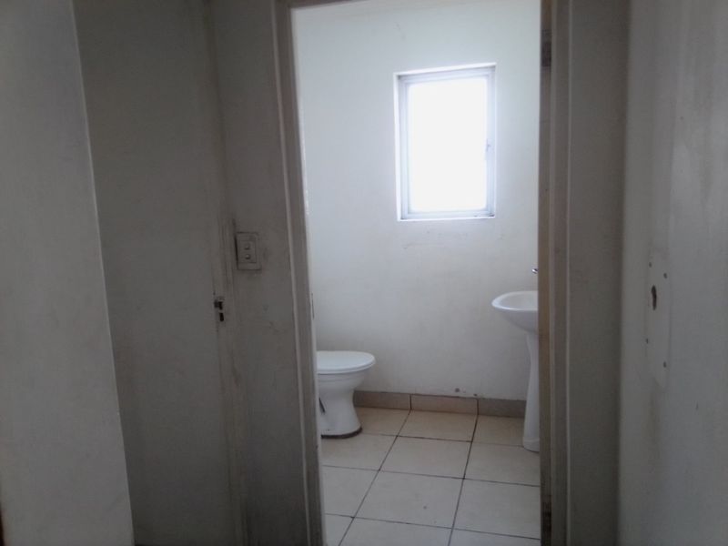 A small, functional bathroom featuring a pedestal basin, toilet, and tiled flooring, requiring cosmetic updates to improve its overall condition.