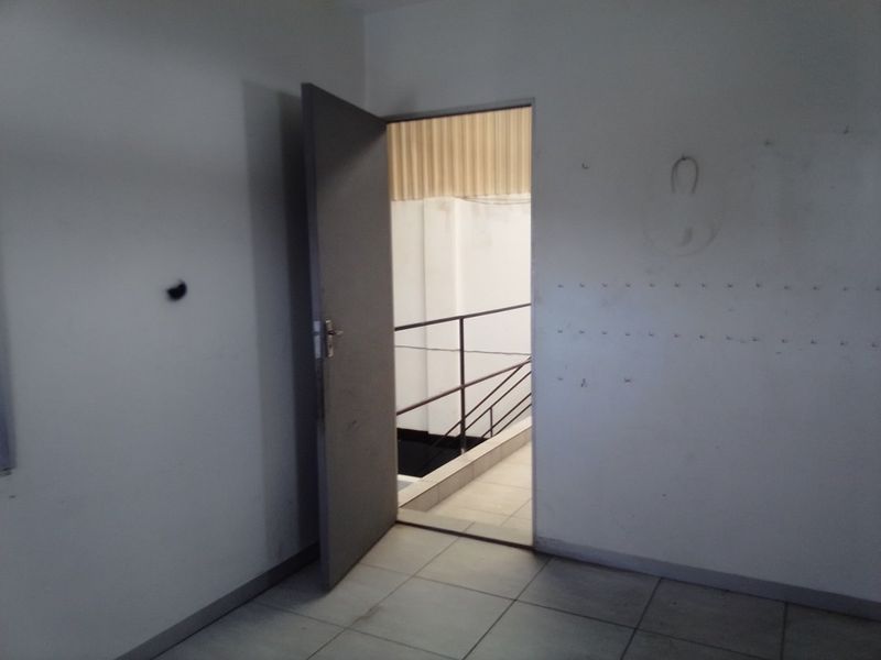 An empty interior hallway featuring tiled flooring and a metal door leading to a staircase with a metal railing.