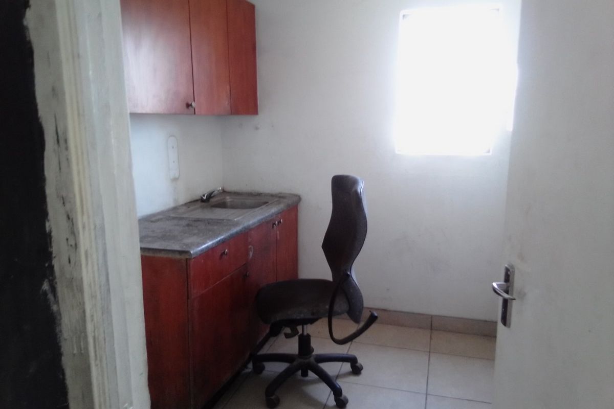 A small utility or scullery area featuring built-in cabinetry, a sink, and tiled flooring, requiring cosmetic updates to improve its overall condition.