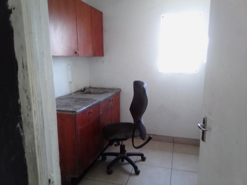 A small utility or scullery area featuring built-in cabinetry, a sink, and tiled flooring, requiring cosmetic updates to improve its overall condition.