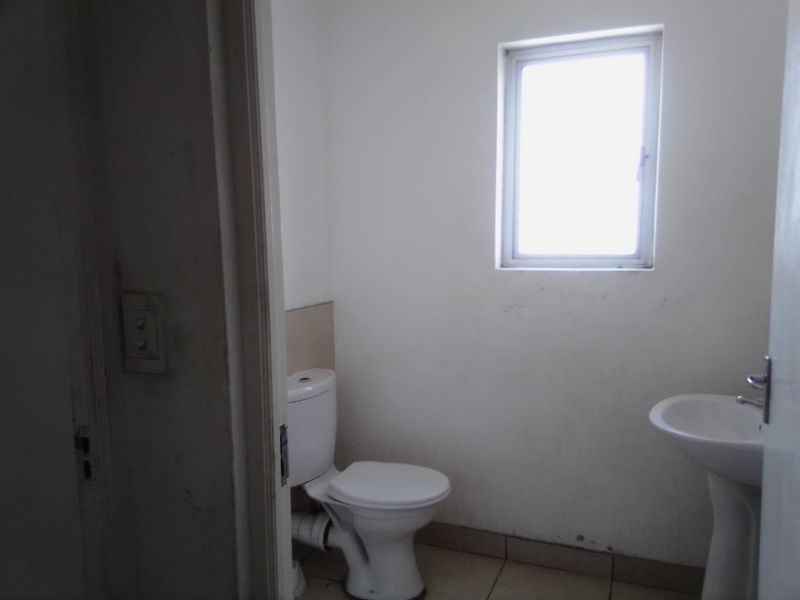 A small, functional bathroom featuring a pedestal basin, toilet, and tiled flooring, requiring minor cosmetic updates to improve its overall appearance.