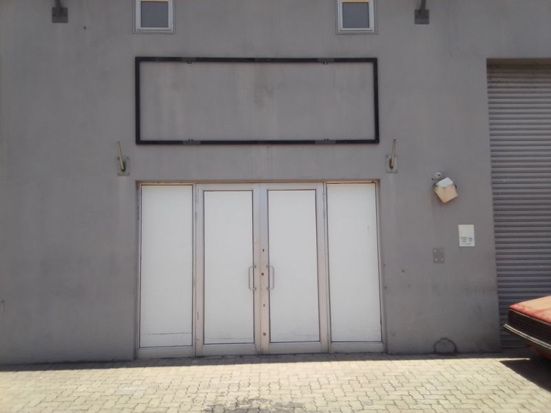 Commercial building facade featuring a double glass entrance door, a roller shutter door, and a dedicated frame for signage.