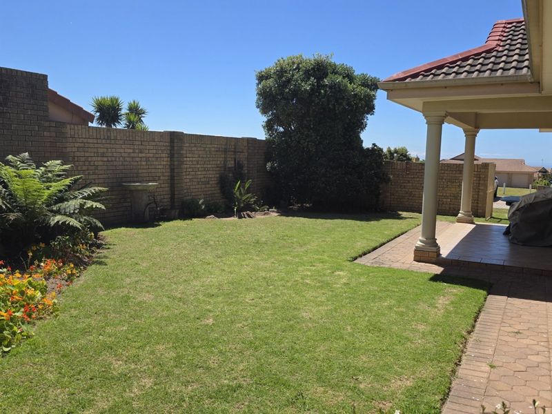 A well-maintained rear garden featuring a paved walkway, a covered patio with concrete columns, and a brick boundary wall.